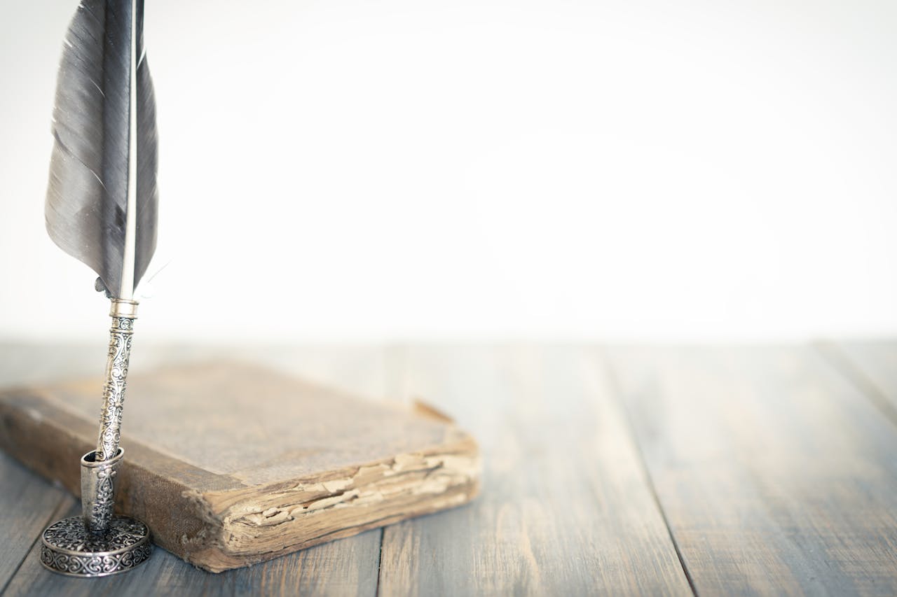 A detailed feather quill beside an aged book on a wooden surface, evoking a classic atmosphere.